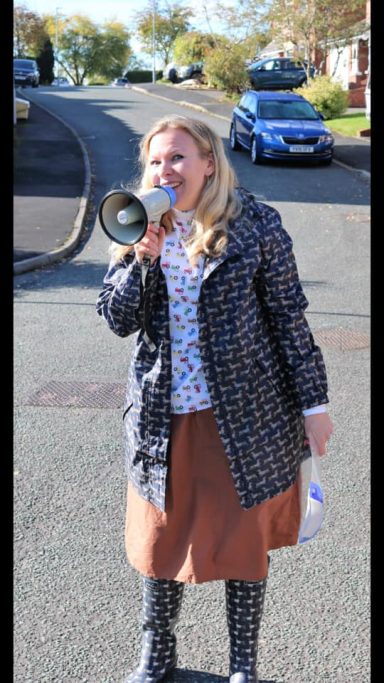 Woman in a coat using a megaphone on a street.